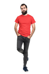 Bearded hipster in red t-shirt standing and balancing on one leg looking away. Full body length...