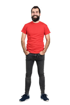 Happy positive friendly bearded man in red t-shirt and tight jeans laughing at camera. Full body length portrait isolated over white studio background.