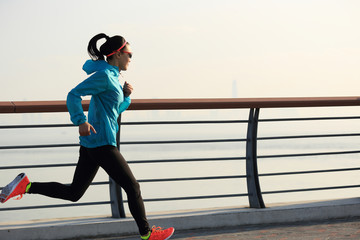 Obraz premium young fitness woman runner running on seaside road