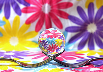 A still life of a glass sphere on a fork with flowers background.
