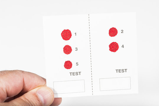 d&eacute;pistage de l'h&eacute;patite B,C et VIH/main tenant un buvard avec cases et gouttes de sang