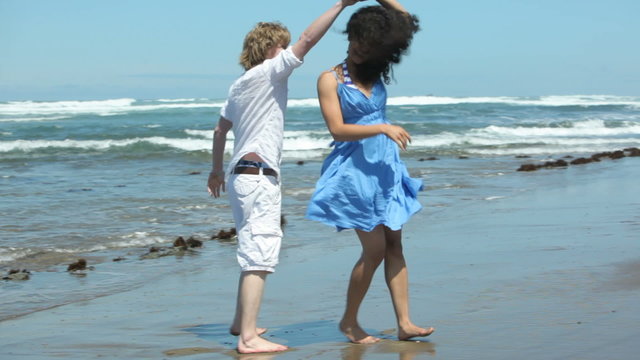 Playful couple walk and dance along beach