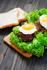 
hearty dinner , filet of beef, beefsteak with fried egg , bread - white toast, lettuce, pepper and spices on a wooden background