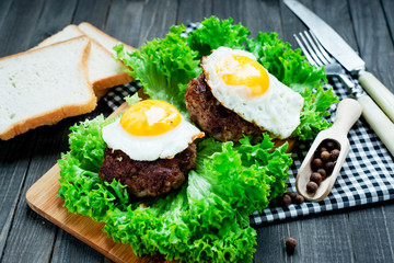 
hearty dinner , filet of beef, beefsteak with fried egg , bread - white toast, lettuce, pepper and spices on a wooden background