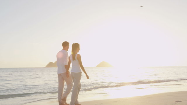 Honeymoon happy married young couple on beach walking in love holding hands at romantic sunrise' Multiracial woman and man relaxing on travel vacation holidays on Lanikai Beach, Oahu, Hawaii, USA  
