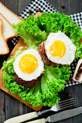 
hearty dinner , filet of beef, beefsteak with fried egg , bread - white toast, lettuce, pepper and spices on a wooden background