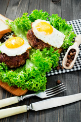 
hearty dinner , filet of beef, beefsteak with fried egg , bread - white toast, lettuce, pepper and spices on a wooden background