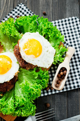 
hearty dinner , filet of beef, beefsteak with fried egg , bread - white toast, lettuce, pepper and spices on a wooden background