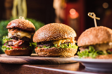 Three juicy tasty burger on the white plate on a dark background - obrazy, fototapety, plakaty