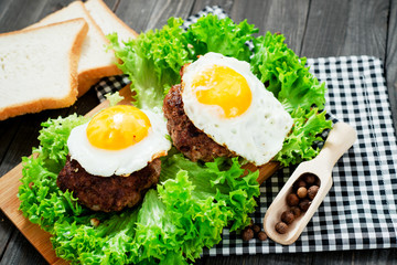 
hearty dinner , filet of beef, beefsteak with fried egg , bread - white toast, lettuce, pepper and spices on a wooden background