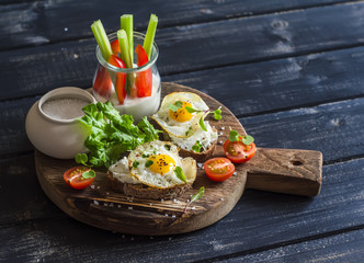 Healthy delicious breakfast or snack -  sandwich with cheese and a fried quail egg, greek yogurt, celery and sweet peppers on rustic wooden board