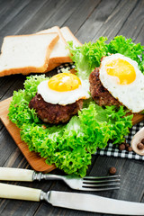 
hearty dinner , filet of beef, beefsteak with fried egg , bread - white toast, lettuce, pepper and spices on a wooden background