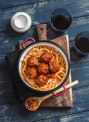 Spaghetti and meatballs in tomato sauce and two glasses with red wine on wooden rustic board. Delicious lunch