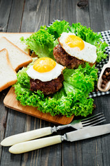 
hearty dinner , filet of beef, beefsteak with fried egg , bread - white toast, lettuce, pepper and spices on a wooden background