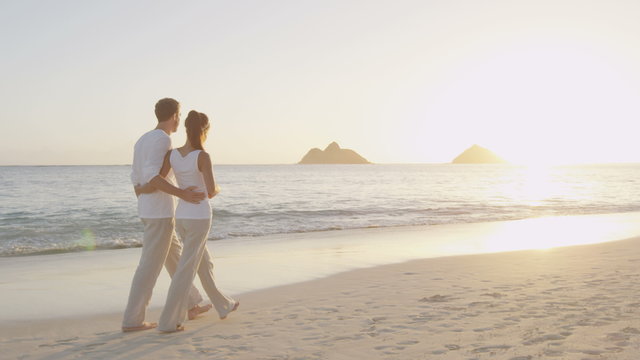 Couple walking on beach taking photo with smart phone at sunrise. Romantic couple taking pictures using smartphone in summer. Woman and man on holidays travel vacation, Lanikai, Oahu, Hawaii, USA. 