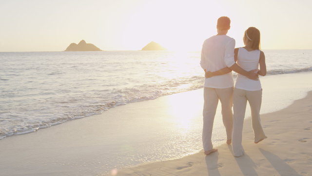 Couple walking on beach enjoying sunrise vacation. Romantic casual couple in love on walk on beautiful summer beach. Woman and man on holidays travel on Lanikai Beach, Oahu, Hawaii, USA. RED EPIC.