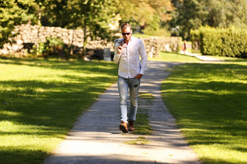 Fototapeta premium An attractive fashion model walking along a path outdoors on a sunny summer day, holding his light blue jacket over his shoulder. 