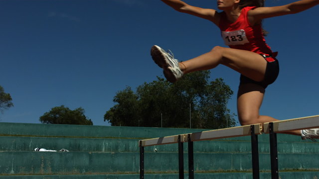 Track athlete jumps over hurdle, slow motion