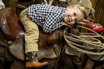Young boy laying on a western cowboy saddle smiling
