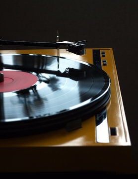 Funny turntable in yellow case with rotation vinyl record with red label isolated on dark background. Vertical photo side view closeup