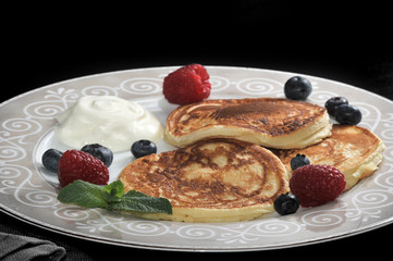 pancakes with sour cream on the plate with raspberries and blueb