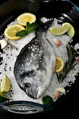 Dorado fish is in glass dish with salt, rosemary, garlic, lime a