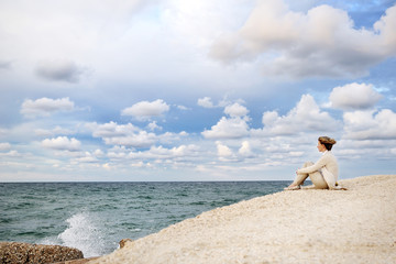 Young woman sitting on the beach looking at the sea and sky