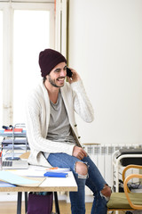 trendy businessman in beanie and cool hipster informal look talking happy on mobile phone