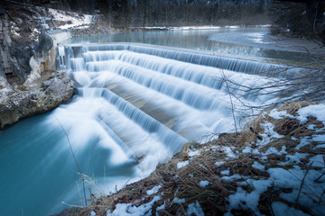flowing water over steps of river fall at winter in bavaria