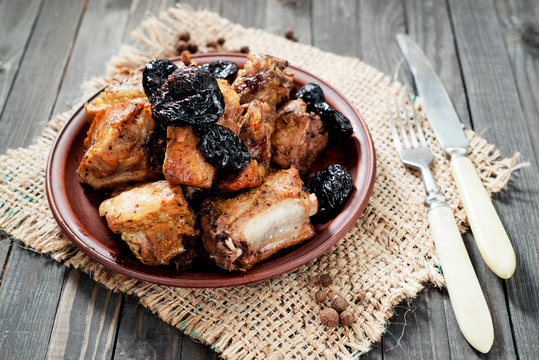 Baked or fried meat , pork ribs with prunes , spices and pepper on a dark wooden background