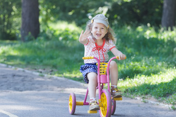 Two year-old laughing girl wearing corduroy flat cap and polka-dotted costume cycling kids pink and yellow tricycle 