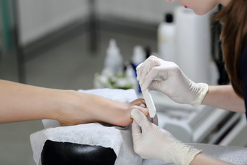 Working with the nail file big toe of clients leg. Service pedicure at the beauty salon.