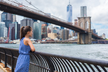 Naklejka premium New York city urban woman enjoying view of Brooklyn bridge and NYC skyline living a happy lifestyle walking during summer travel in USA. Female Asian tourist in her 20s.