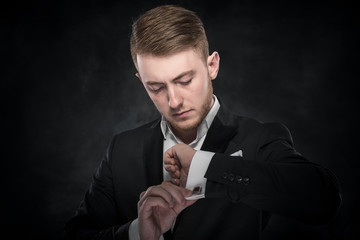 Elegant young fashion man looking at his cufflinks.