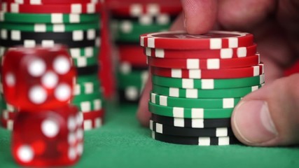 Red dice and casino chips in fingers on green table