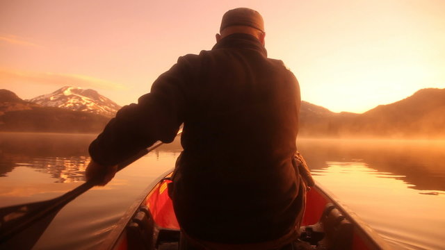 Man paddling canoe at sunrise