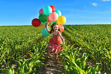 happy little girl in red dress running with balloons on green corn field © ramonki
