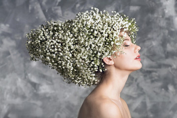 Portrait of young woman with hairstyle made of white baby flowers on gray background