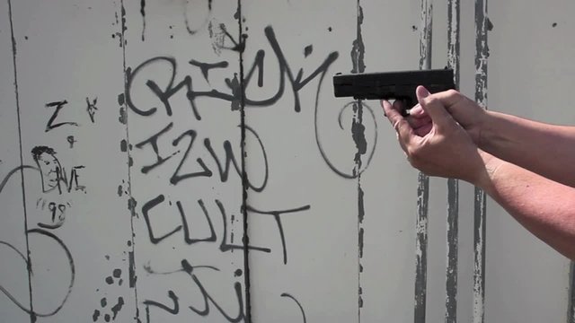 Man's hands holding automatic pistol, discharging entire clip against battered steel wall background