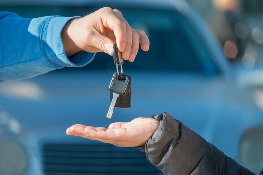 car seller gives car keys to new car owner - car rental customer and salesman  -  rent a car car ownership concept 