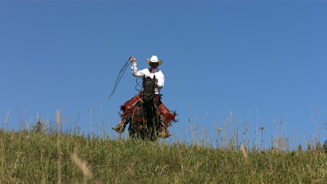 Cowboy rides over hill swinging lasso, slow motion