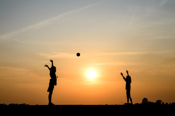 silhouette of boy and girld plying ball on sunset background
