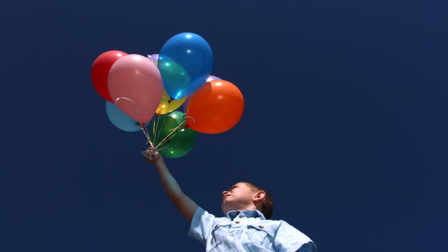 Young boy lets balloons go into sky, slow motion