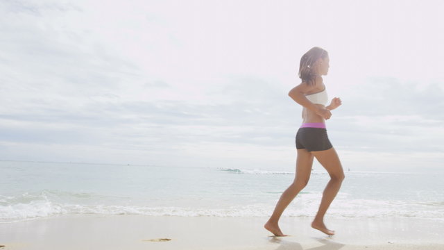 Confident young woman running on sea shore. Determined female is in sportswear. Jogger is exercising on sunny day. Idyllic view of seascape against sky.