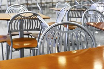 Chairs and tables in fast food restaurant, cafe silver steel furniture with orange wooden seats and working surfaces, food court, nutrition industry, selective focus 
