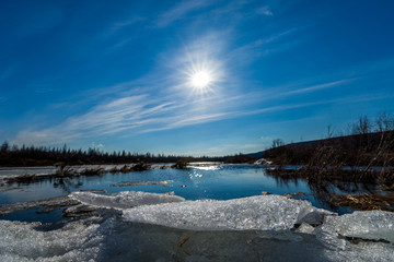 Spring landscape with river, ice, cloudy sky and sun 
