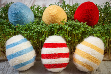 Easter eggs wrapped woolen string and green cress on wooden background, decoration for Easter