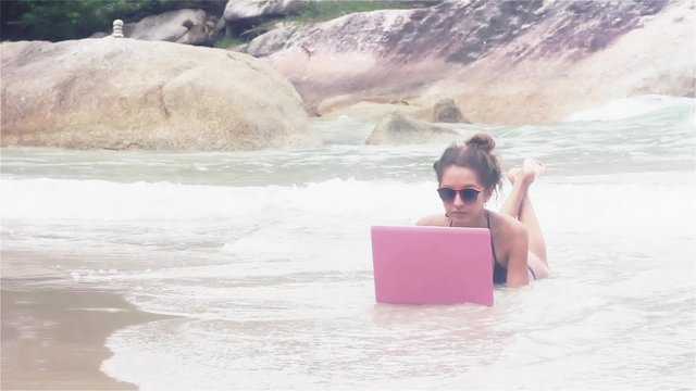 Woman is laying in the sea on the beach with laptop covering with water