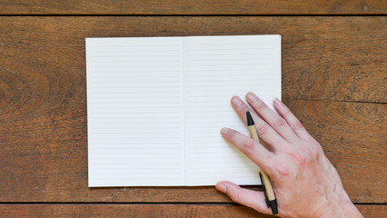 Obraz premium Man hands with pen writing on empty notepad over wooden table.