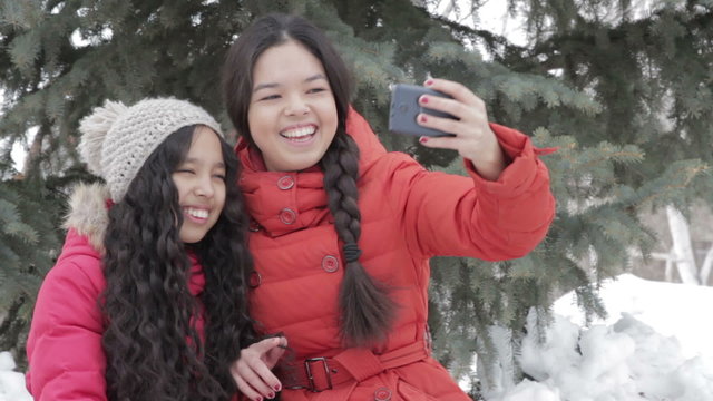 Smiling two girl taking a selfie with smartphone outdoors in warm clothes
